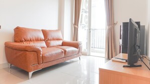 A modern living room with a leather sofa, a flat-screen TV, and a balcony with curtains. - Comfort And Good Choice 2Br Signature Park Grande Apartment (Jakarta)