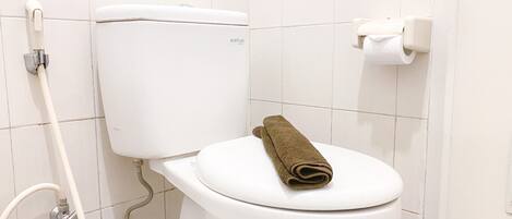 A white toilet with a brown towel on the seat, a flush handle, and a paper towel dispenser.