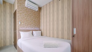A neatly made bed with white linens and pillows, a wooden headboard, and a white towel on the bed. - Elegant And Comfy 2Br At Transpark Cibubur Apartment (Depok)