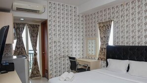 A hotel room with a bed, a desk, a chair, a mirror, and a window with curtains. - Comfy And Tidy Studio Apartment At Margonda Residence 4 Near Ui (Depok)