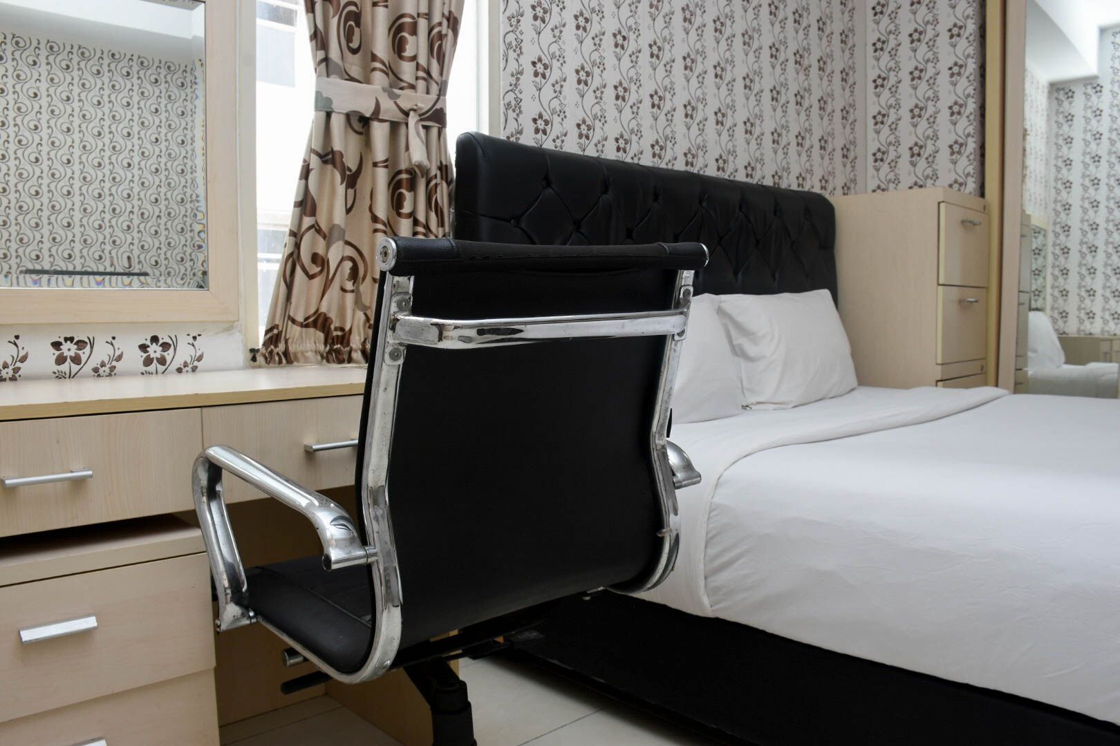 A modern bedroom with a black upholstered chair, a bed with white bedding, and a dresser with a mirror.