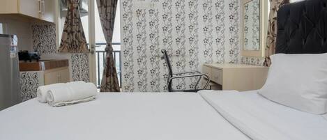 Habitación de hotel con cama, escritorio, silla, espejo y kitchenette.