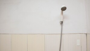 A shower with a handheld showerhead and a flexible hose against a wall with vertical paneling. - Comfy And Tidy Studio Apartment At Margonda Residence 4 Near Ui (Depok)