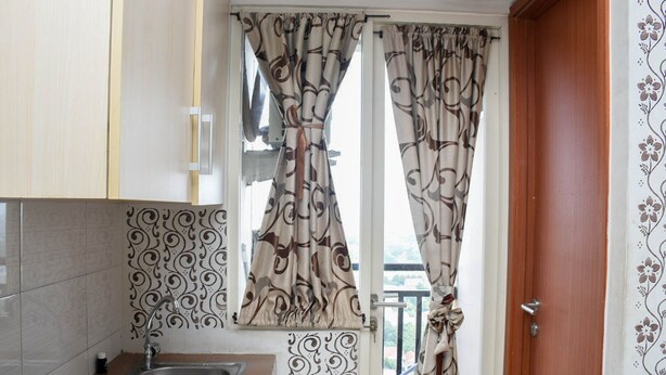A kitchen with a gas stove, a sink, patterned tiles, and curtains with a swirl design. - Comfy And Tidy Studio Apartment At Margonda Residence 4 Near Ui (Depok)