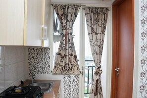 A kitchen with a gas stove, a sink, patterned tiles, and curtains with a swirl design. - Comfy And Tidy Studio Apartment At Margonda Residence 4 Near Ui (Depok)