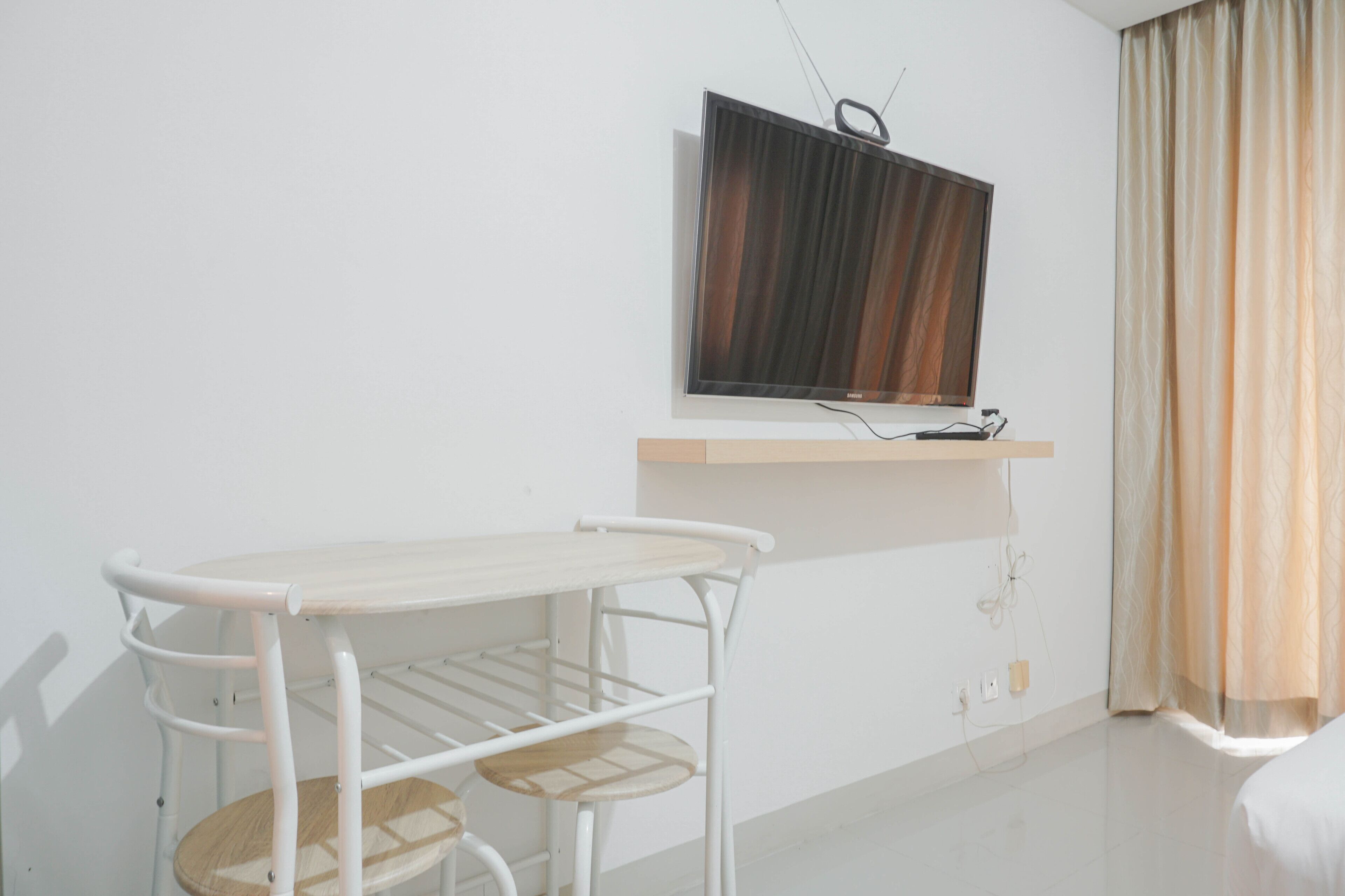 Ein Zimmer mit einem Bett, einem an der Wand befestigten Fernseher, einem kleinen Tisch und einem Sessel.