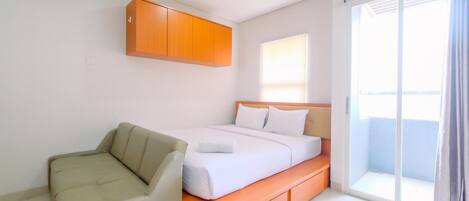 A modern hotel room with a bed, a sofa, a wooden cabinet, and a sliding glass door to a balcony.