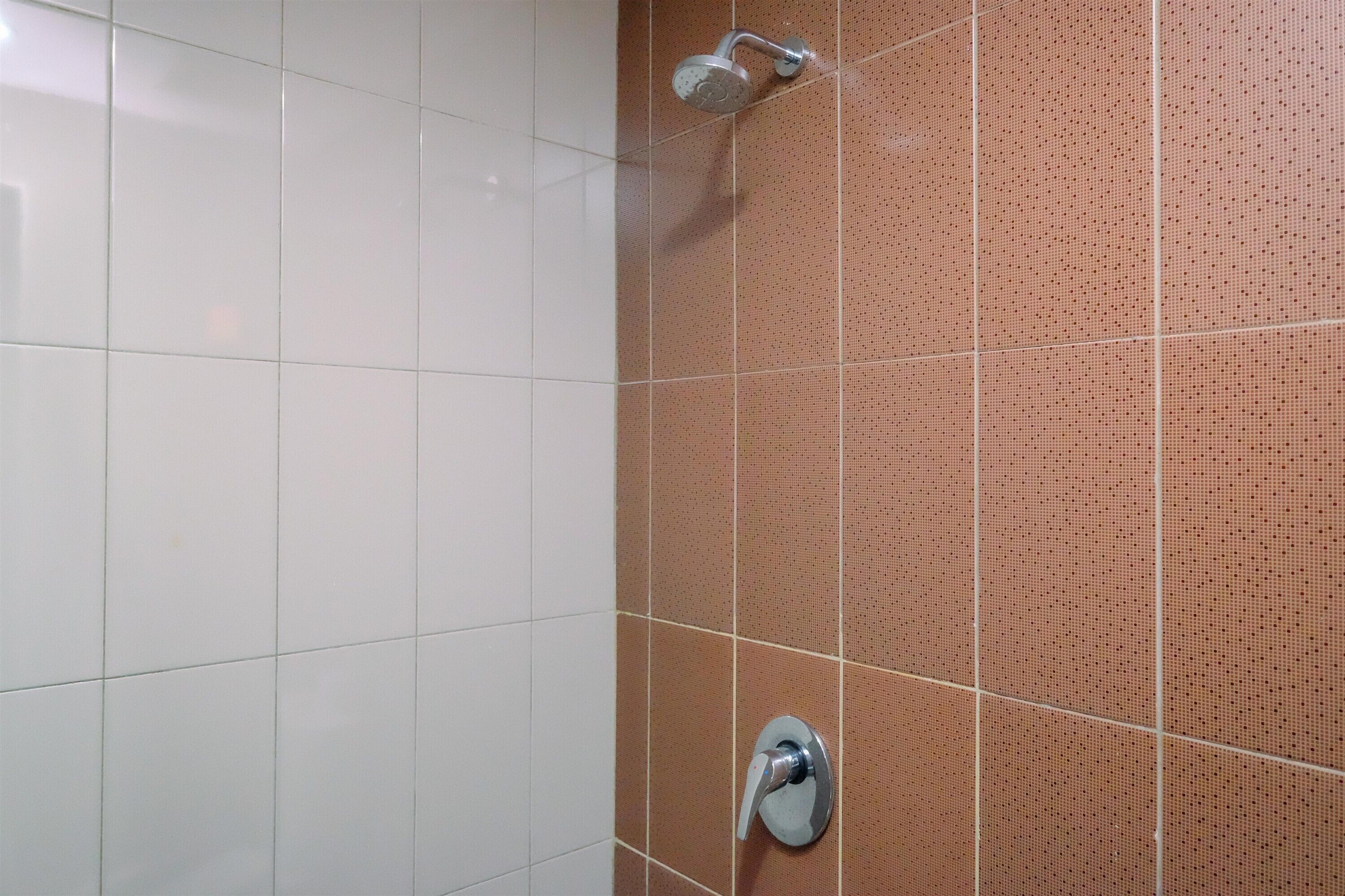 Un baño con paredes de azulejos blancos y marrones, un cabezal de ducha y un grifo.