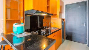 A kitchen with orange cabinets, a black countertop, a gas stove, a sink, and a refrigerator. - Minimalist And Nice Studio Apartment Atlanta Residence (Depok)