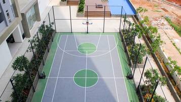 Una cancha de baloncesto al aire libre con aro, rodeada por una valla y follaje.