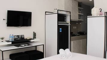 Una habitación de hotel moderna con televisión de pantalla plana, minibar, microondas y pequeña cocina.