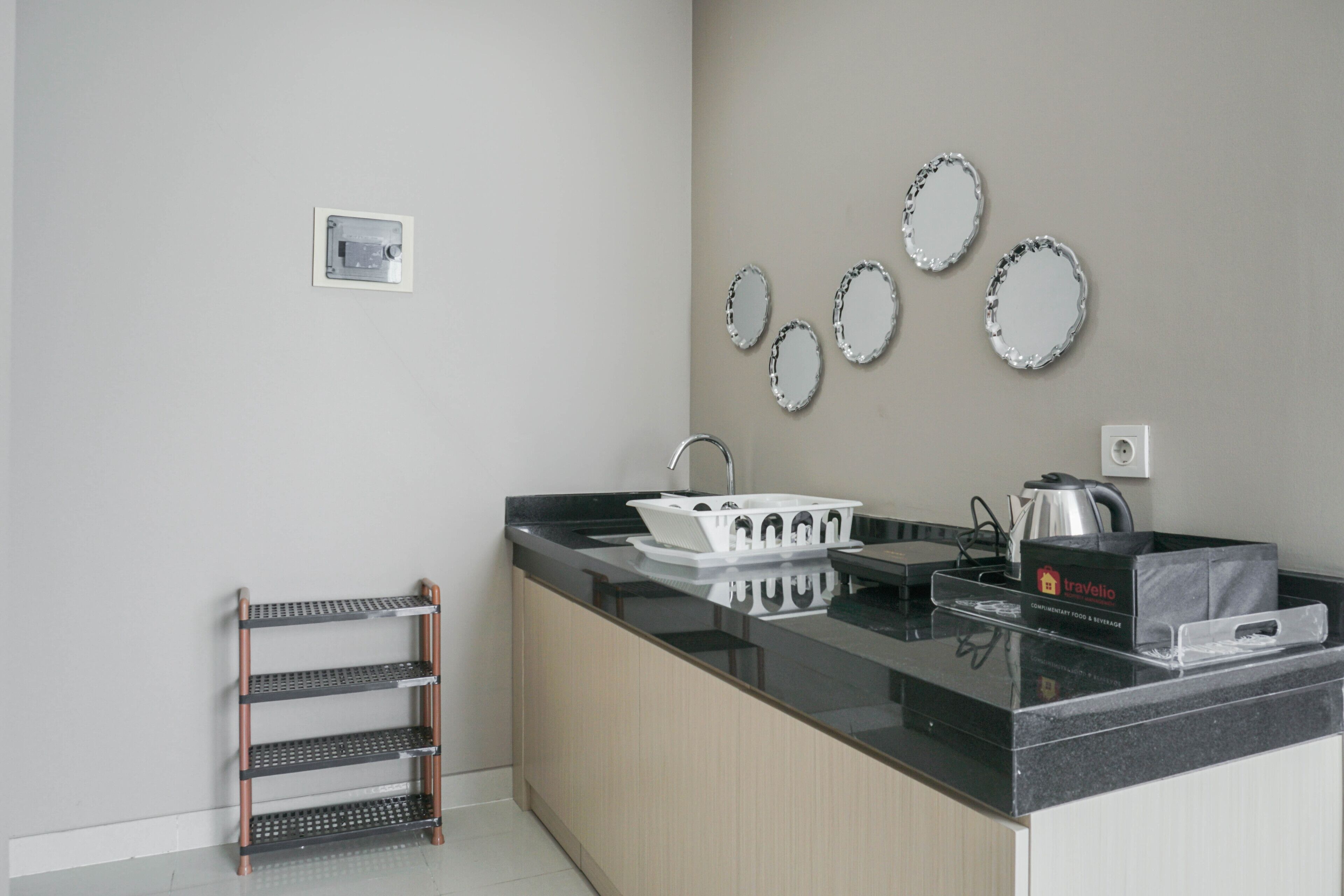 A modern kitchen with a black countertop, a sink, and a coffee maker. There are three shelves with storage baskets and a small rack with hanging items.