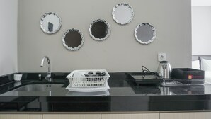 A kitchen with a black countertop, a sink, and a dish rack. There are four mirrors on the wall. - Chic And Cozy Studio Apartment At Ciputra International (Jakarta)