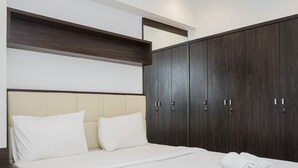 A modern bedroom with a large bed, dark wooden wardrobe, and a beige headboard.