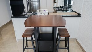 A kitchen with a central island, two stools, a sink, and a refrigerator.