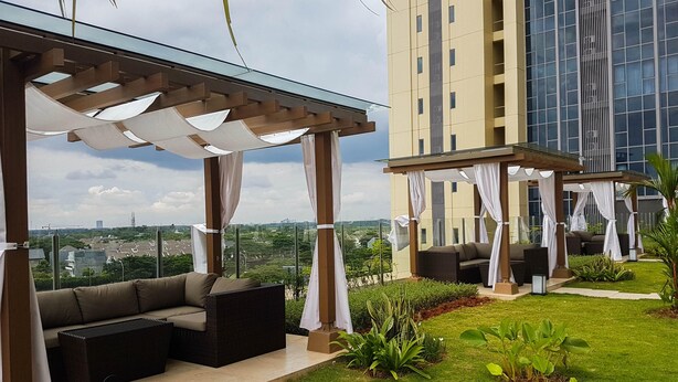 A modern outdoor lounge area with a glass ceiling, cushioned seating, and a view of a cityscape.