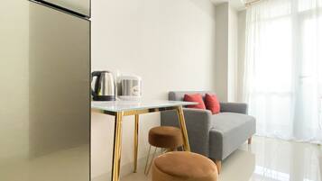 Un salon moderne avec une table à plateau en verre, deux poufs marron, un canapé gris avec des coussins rouges et une machine à café.