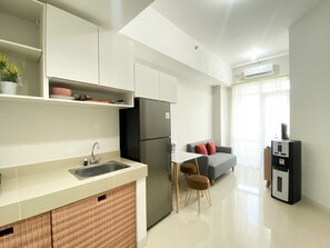 Eine moderne Küche mit einem schwarzen Kühlschrank, weißen Schränken und einer Spüle. Ein Essbereich mit einem weißen Tisch und zwei Stühlen ist vorhanden. Ein graues Sofa mit roten Kissen ist im Hintergrund zu sehen.