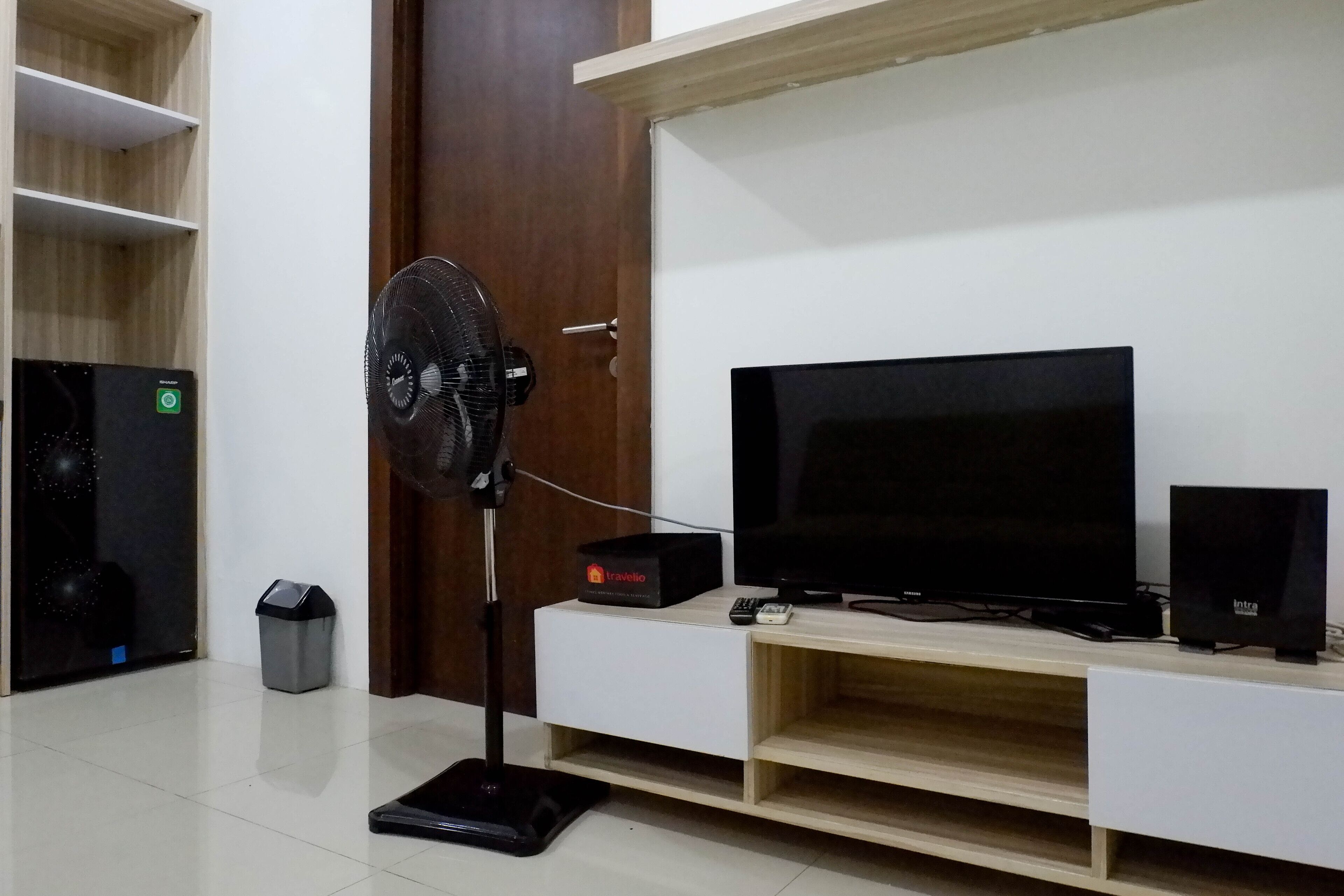 A room with a TV, a fan, a trash bin, and a small heater.