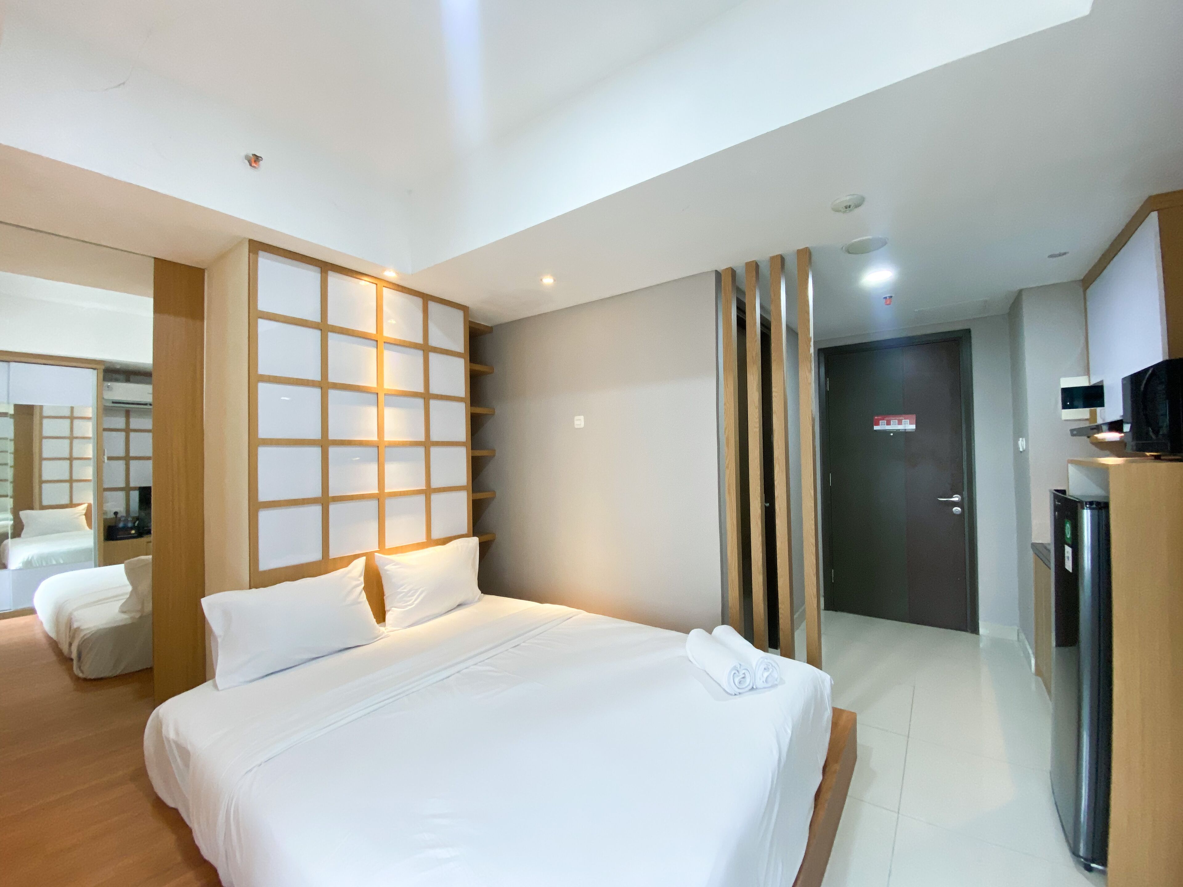 Une chambre d’hôtel avec un grand lit, une tête de lit en bois, un miroir, une armoire et une porte.