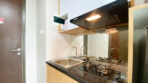 A compact kitchen with a gas stove, a sink, and a stainless steel refrigerator. - Nice Studio Apartment At Pollux Chadstone (Cikarang)