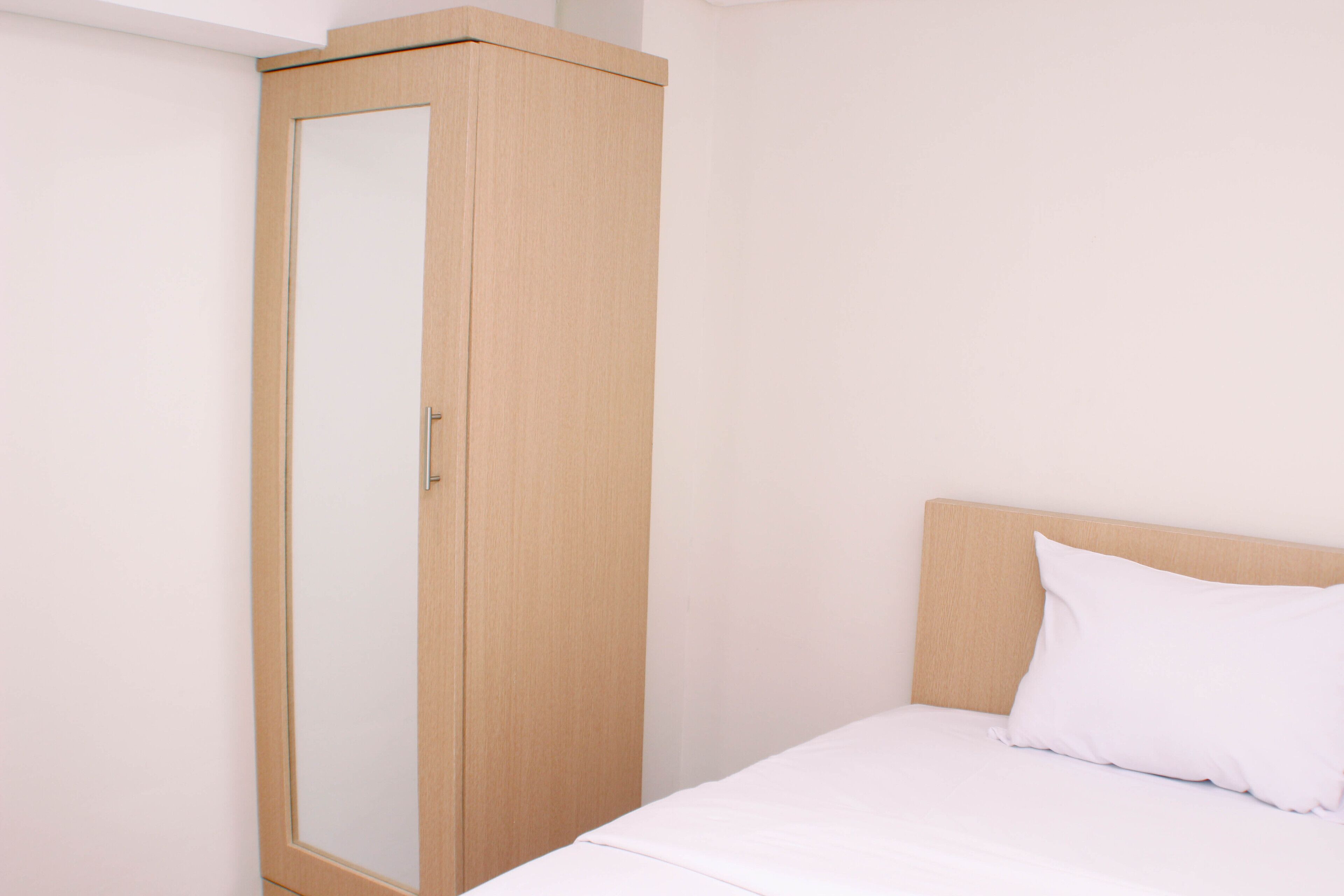 A bedroom with a wooden wardrobe, a bed with white bedding, and a plain wall.