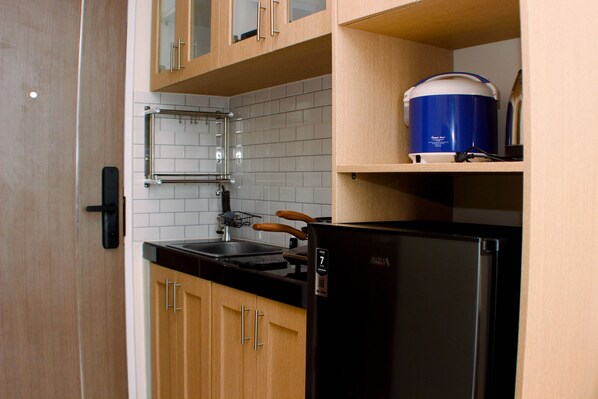 Une cuisine avec des meubles de rangement en bois, un réfrigérateur noir, un distributeur d’eau bleu et un évier en acier inoxydable.