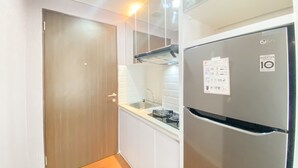 Une cuisine de taille réduite, dotée d’un réfrigérateur en acier inoxydable, de meubles blancs et d’une porte en bois.