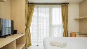Une chambre d’hôtel avec un lit, un téléviseur posé sur une étagère en bois et une fenêtre avec des rideaux.