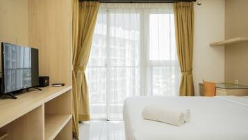 A hotel room with a bed, a TV on a wooden shelf, and a window with curtains.