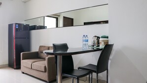 A compact room with a sofa, a dining table with chairs, a refrigerator, and a coffee maker. - Comfort And Cozy Stay 2Br At 29Th Floor Transpark Cibubur Apartment (Depok)