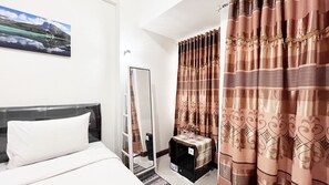 A hotel room with a bed, a mirror, a small table with a checkered tablecloth, and curtains with a pattern. - Compact Studio Room Apartment Vida View Makassar (Makassar)