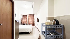 A hotel room with a bed, curtains, a TV, and a laundry basket. - Compact Studio Room Apartment Vida View Makassar (Makassar)