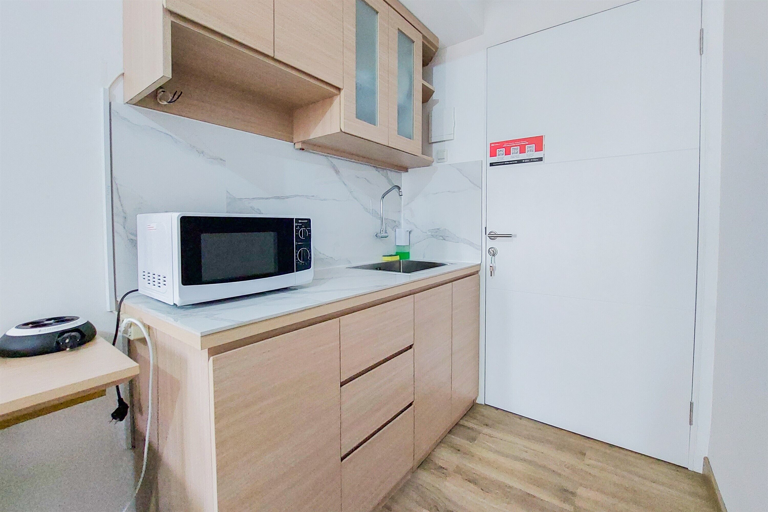 Een kleine keuken met een magnetron, spoelbak en houten kastjes.