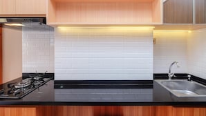 A modern kitchen with white subway tiles, a black countertop, stainless steel sink, and wooden cabinets. - Nice And Fancy Studio At Transpark Cibubur Apartment (Depok)