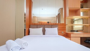 A hotel room with a bed, a desk, and a mirror. - Nice And Fancy Studio At Transpark Cibubur Apartment (Depok)