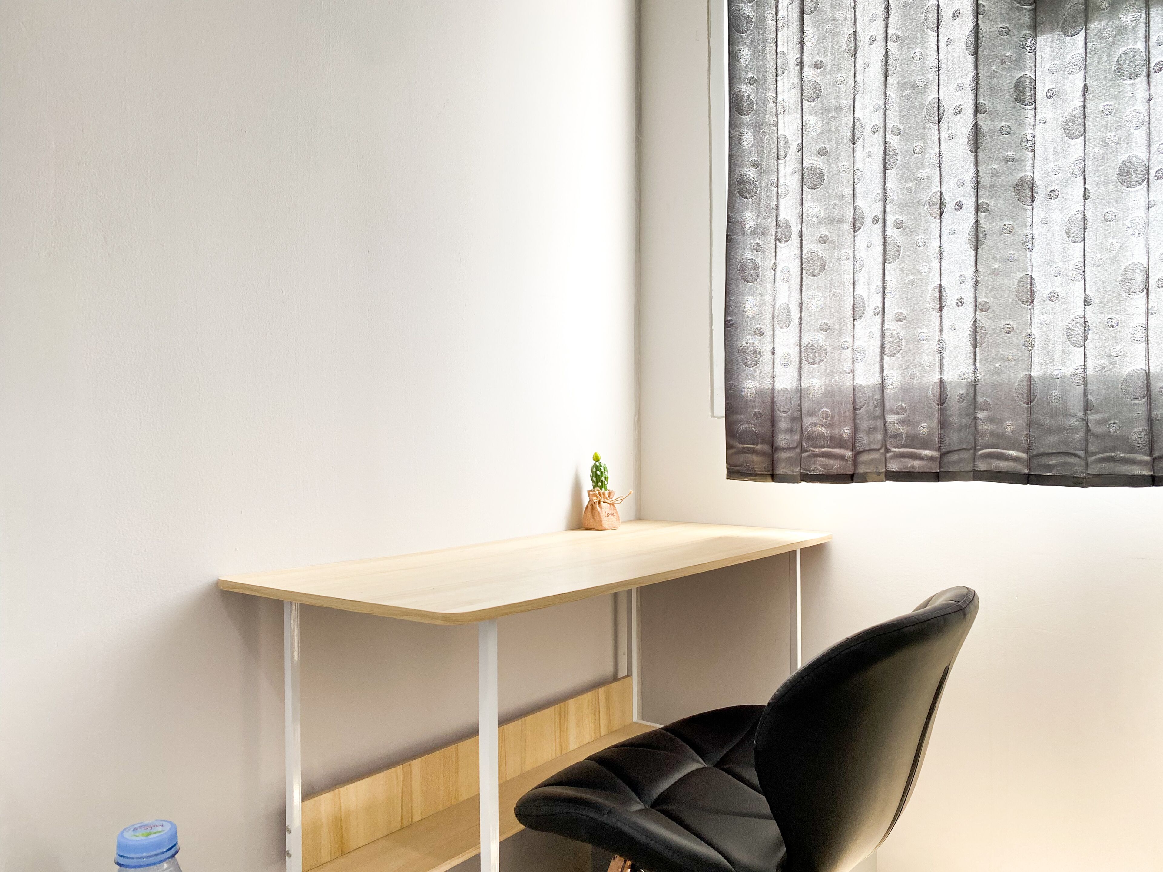 A corner room with a wooden desk, a black chair, a small cactus, and a bottle of water.