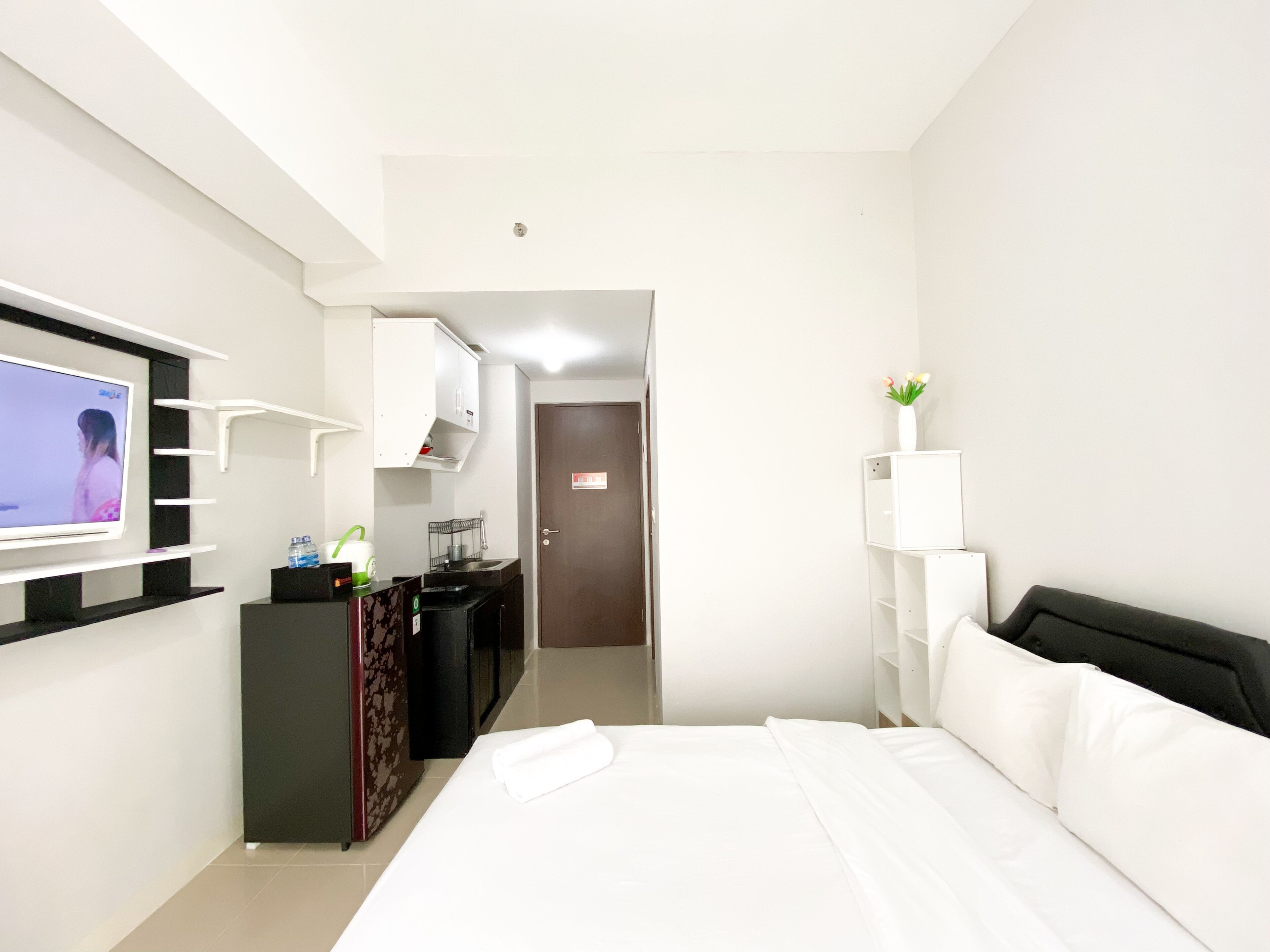 A hotel room with a bed, a TV on the wall, a desk with a chair, and a door leading to another room.