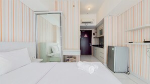 Ein Hotelzimmer mit einem Bett, einem kleinen Schreibtisch, einem Kühlschrank und gestreifter Tapete.