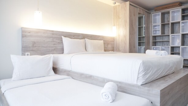 Habitación de hotel con dos camas, cabecero de madera y armario empotrado con puertas de vidrio.