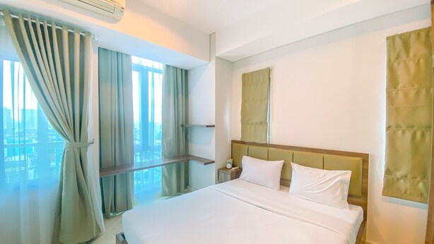 A hotel room with a large bed, a nightstand, a window with curtains, and a city view. - Best Location 2Br Apartment At Capitol Park Residence (Jakarta)