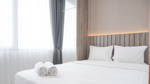 Een netjes opgemaakt bed met witte lakens en opgerolde handdoeken, een houten hoofdbord en een raam met dunne gordijnen.