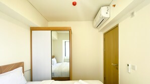 Ein Hotelzimmer mit Bett, Holztür, Klimaanlage und Spiegel, der eine Person im angrenzenden Raum reflektiert.