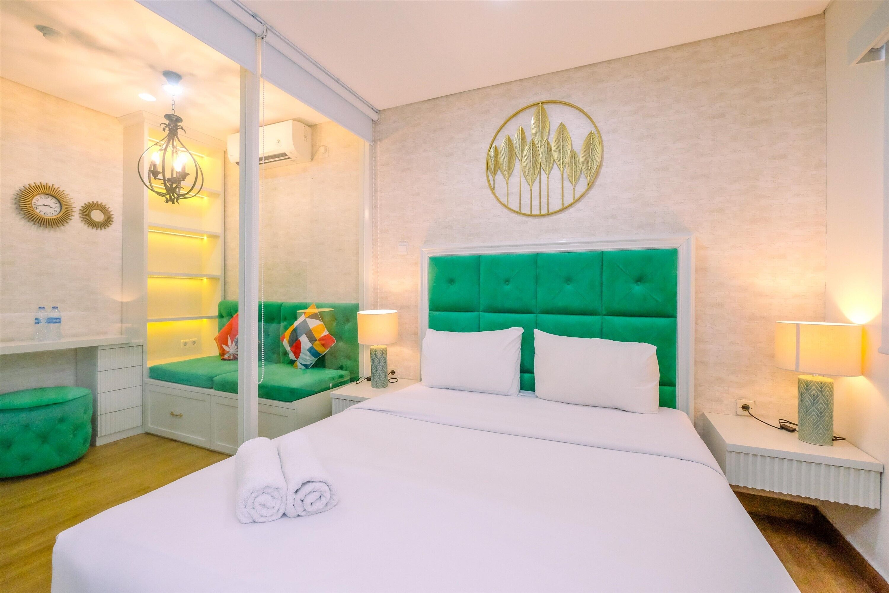 Une chambre d’hôtel avec un grand lit, une tête de lit recouverte d’un tissu vert, une table de chevet avec une lampe et un miroir.