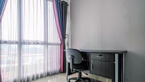 A room with a desk, chair, and large windows with sheer curtains. - Homey Studio Room At Taman Melati Margonda Apartment (Depok)