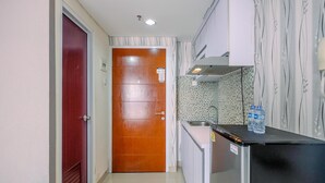 A compact kitchen with a wooden door, a sink, and a refrigerator. - Homey Studio Room At Taman Melati Margonda Apartment (Depok)