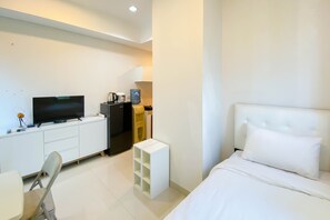 Relax in a serene space with a large flat-screen TV, a comfortable bed, and a small storage unit.