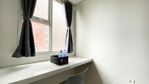 A small, bright room with a window, a desk, and a chair. There are two bottles of water on the desk. - Nice And Cozy Studio At Transpark Juanda Bekasi Timur Apartment (Bekasi)