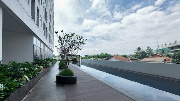 A modern building with a long, narrow outdoor area featuring a wooden deck and planters with greenery.