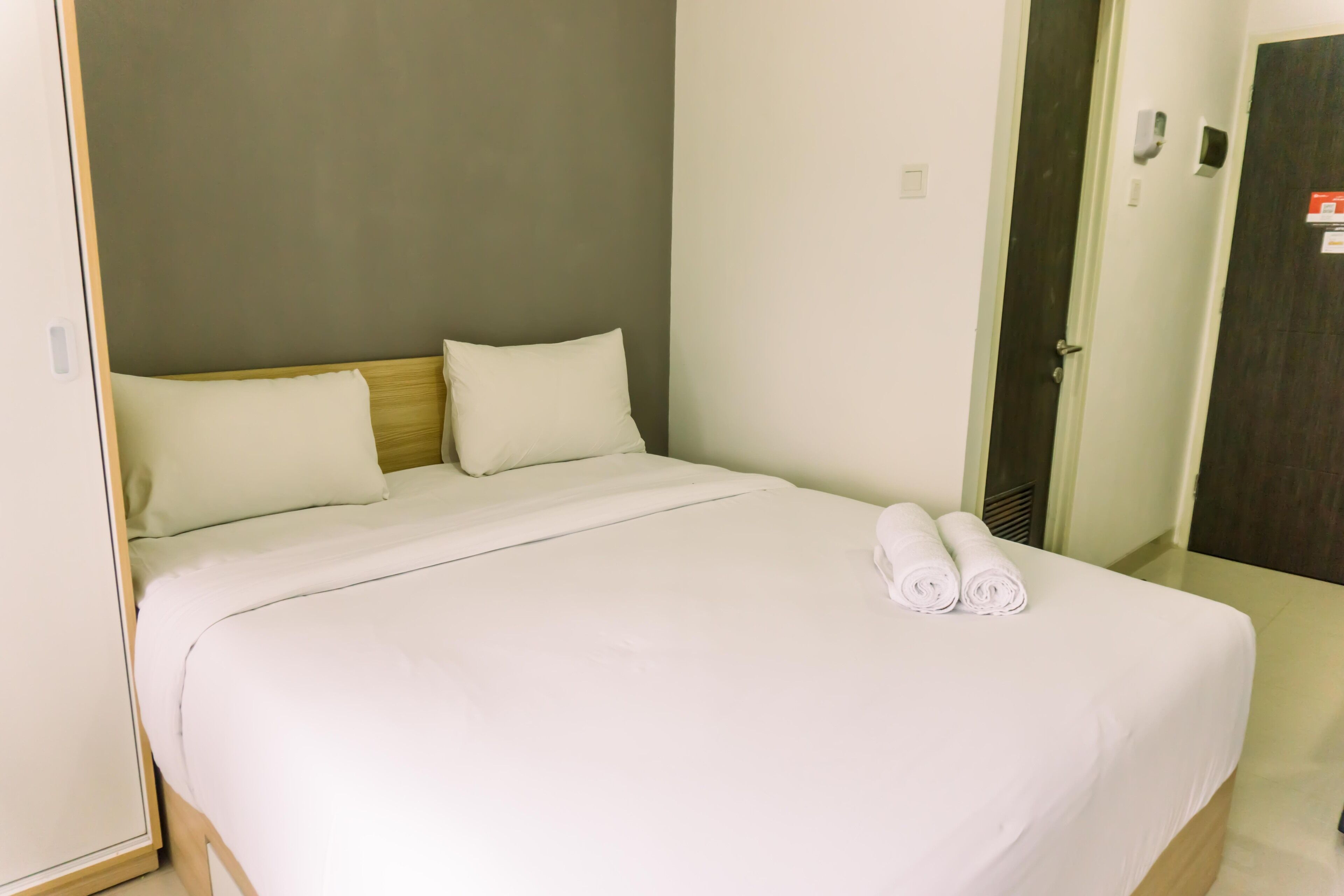 A neatly made bed with white linens and two rolled towels on the side.